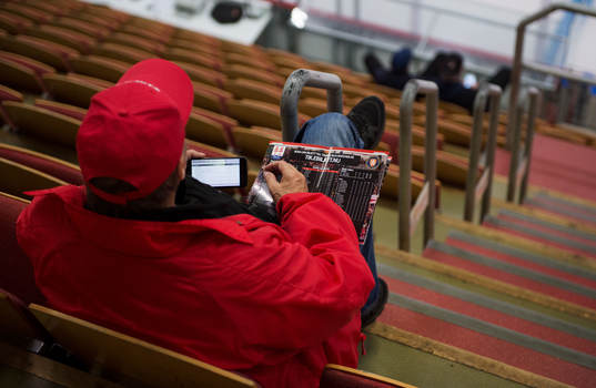 En man i publiken med ett matchprogram och en telefon