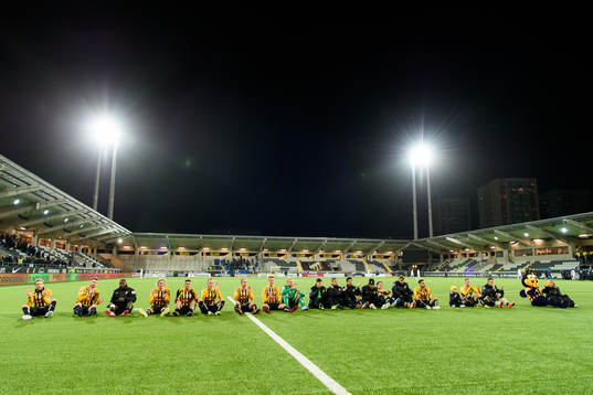 Häckens spelare sitter på planen framför supportrarna