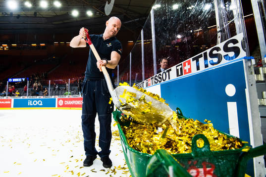 A janitor shuffles gold glitter into a wheelbarrow