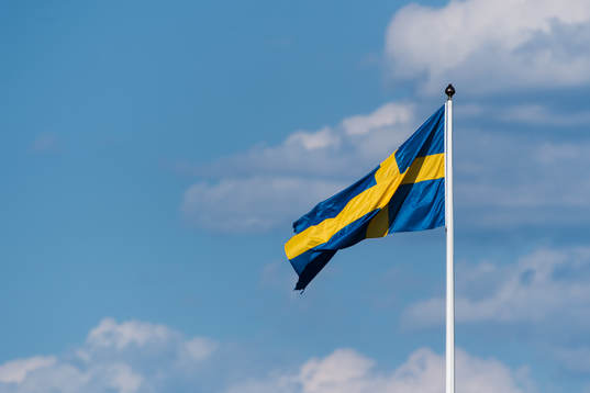Svenska flaggan på en flaggstång med blå himmel och moln