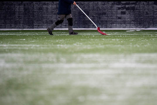 A man shuffles snow from the pitch