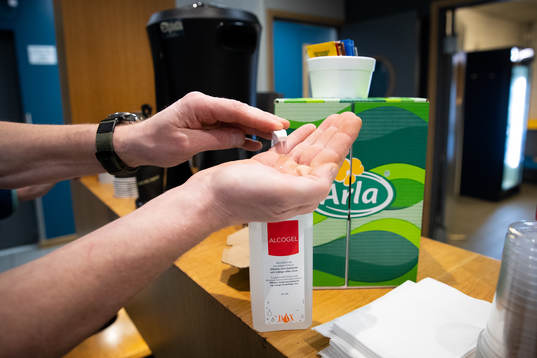 En person spritar sina händer i pressrummet innan