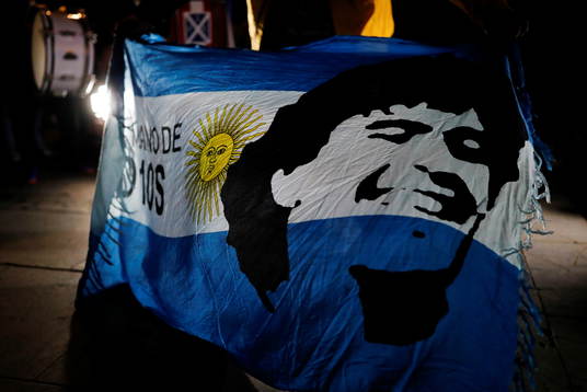 A soccer fan holds an Argentine flag with the face of late
