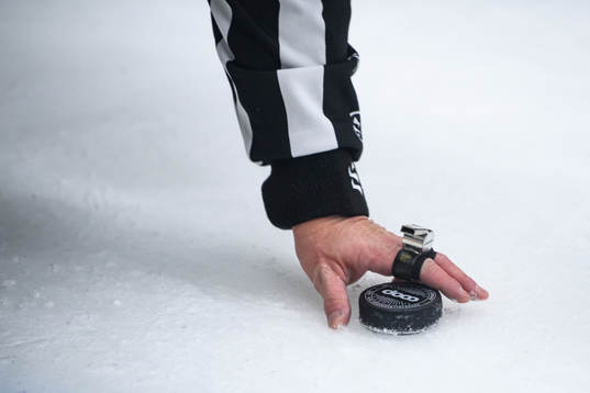 En domare tar upp en puck från isen