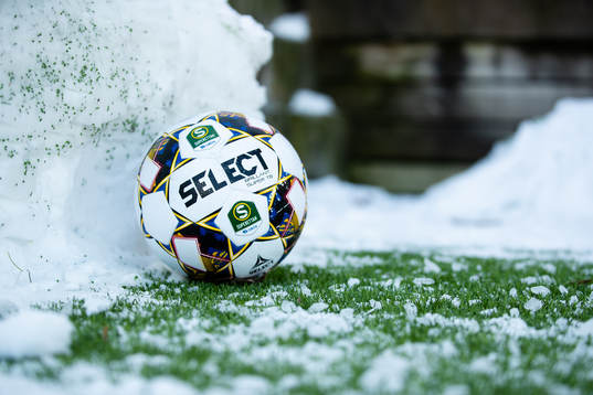 En fotboll vid en snövall bredvid planen