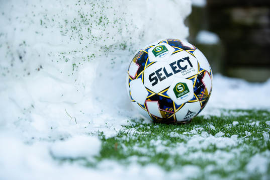 En fotboll vid en snövall bredvid planen
