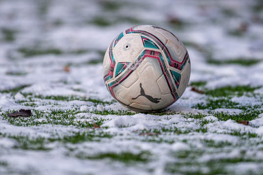 En fotboll ligger på en snöig konstgräsplan