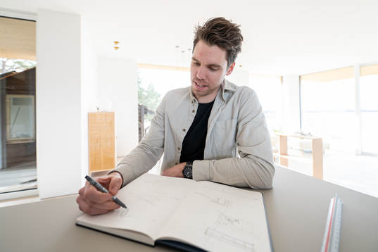 Linus Fernström sitter och skissar i en skissbok han fått