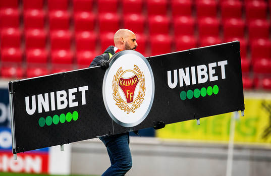 En funktionät bär på en Unibetskyltunder fotbollsmatchen