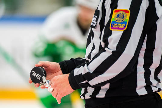En domare håller i sin visselpipa och en matchpuck