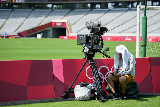 A cameraman with a towel over his head to shield from heat