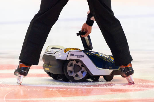 Domaren plockar upp matchpucken ur en robotgräsklippare