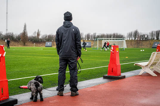 En förälder står och tittar ut över träningsplanen