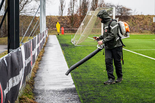 En planskötare blåser bort löv och konstgräsgranulat
