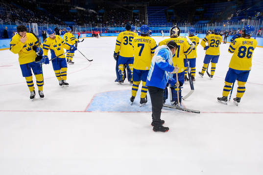 A volunteer tries to clean the ice as the players of Sweden