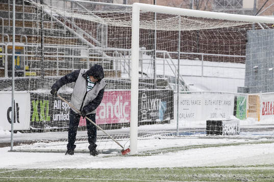 Funktionärer sopar av planen innan fotbollsmatchen i