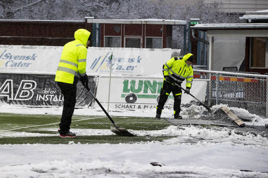 Funktionärer skottar snö innan fotbollsmatchen i