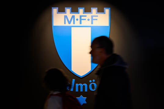 En person passerar Malmö FFs logotype i shopen