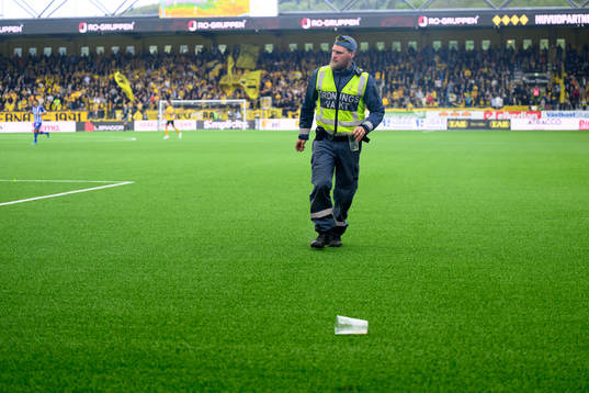 En ordningsvakt plockar upp inkastade föremål från planen