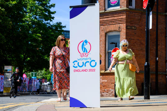 Bystanders pass billboards for the UEFA Women's Euro 2022