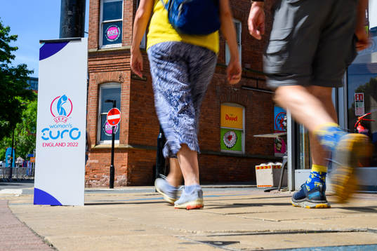 Bystanders pass billboards for the UEFA Women's Euro 2022