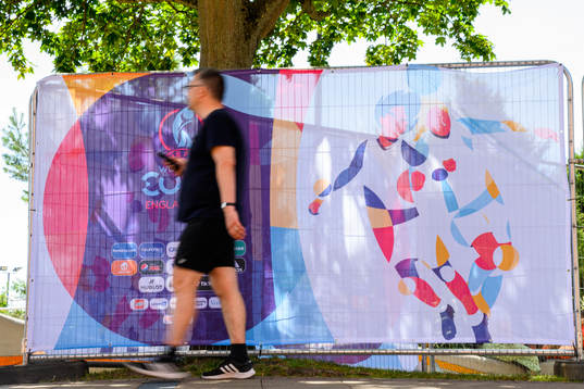 Bystanders pass billboards for the UEFA Women's Euro 2022