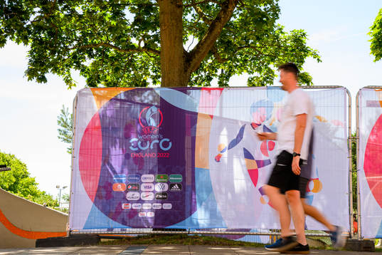 Bystanders pass billboards for the UEFA Women's Euro 2022