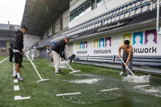 Funktionärer skrapar bort vatten från planen