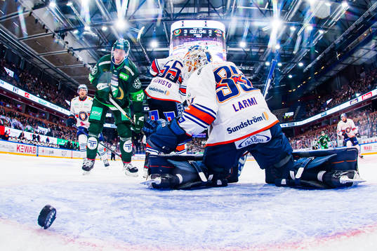 En puck bakom Växjös målvakt Emil Larmi och Färjestads
