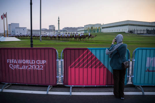 A woman takes photos of camels riding in front of