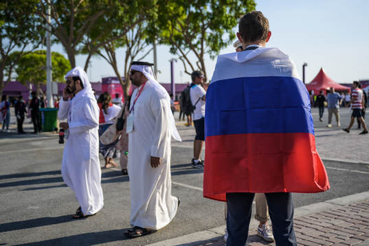 Men in traditional Qatari clothing pass by a man wearing a
