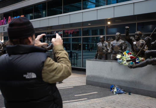 A passerby takes a photo of a memorial at a statue of the