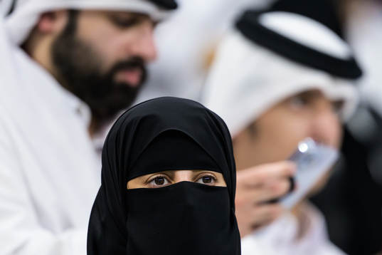 A woman wearing a niqab in front of two men in Qatari