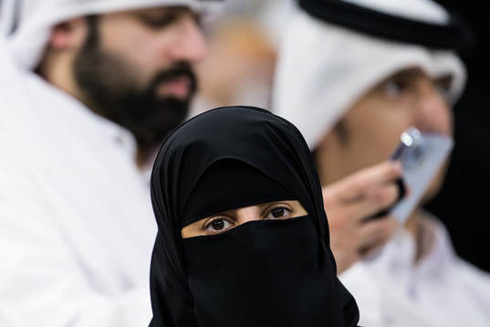 A woman wearing a niqab in front of two men in Qatari