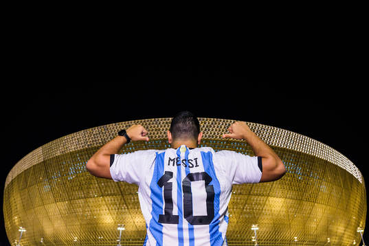 A man with a Lionel Messi jersey poses in front of Lusail