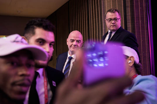Two members of media take selfies with Gianni Infantino,