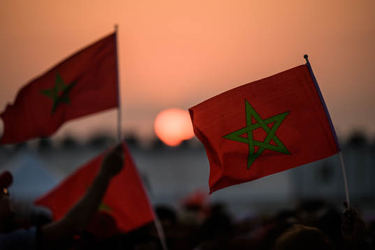 People wave Moroccan flags at sunset