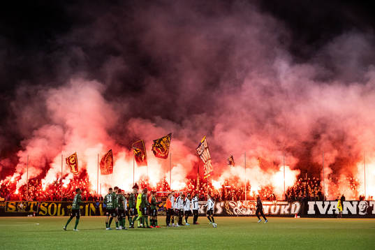 Varbergs och AIKs spelare framför supportar med bengaliska