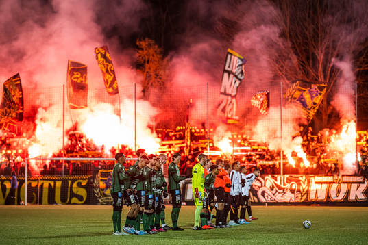 Varbergs och AIKs spelare framför supportar med bengaliska