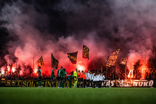 Varbergs och AIKs spelare framför supportar med bengaliska