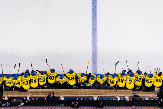 Players of Sweden leaning towards the ice from the bench at