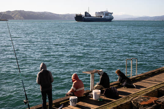 People fish as a ferry pass by