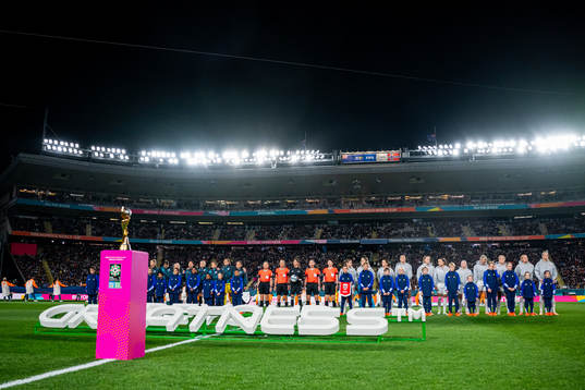 Players of both teams line up behind the trophy