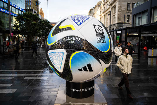 People walk past a replica of the official match ball