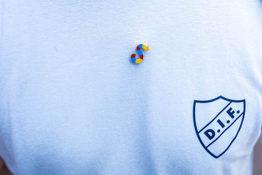 En pin med ett S i Djurgårdens färger på en t-shirt