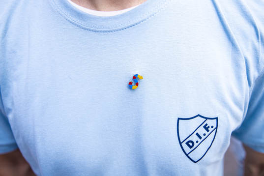 En pin med ett S i Djurgårdens färger på en t-shirt