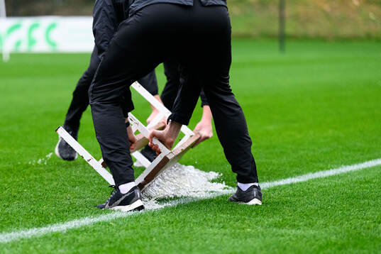 Staff of Brann shuffels water of the pitch