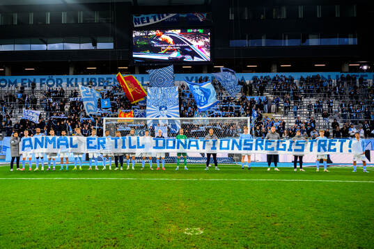 Malmö FF spelare med banderoll framför klacken