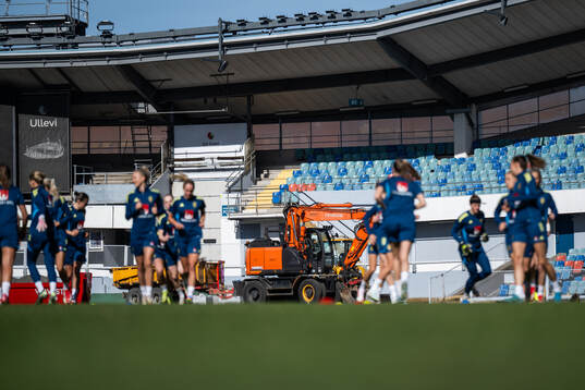 An excavator is seen behind players
