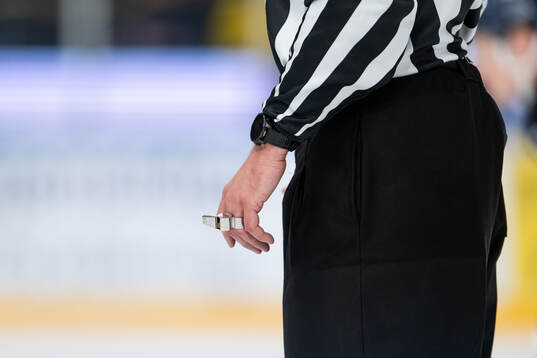 A hand of a referee holds a whistle